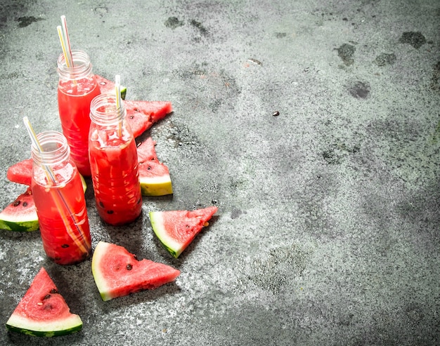 Wassermelonensaft in Flaschen mit Strohhalmen auf rustikalem Tisch.