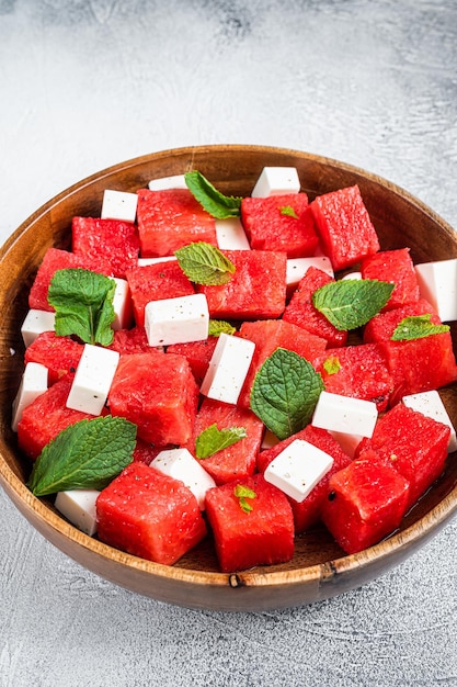 Wassermelonensalat mit Fetakäse in einer Holzplatte. Weißer Hintergrund. Ansicht von oben.