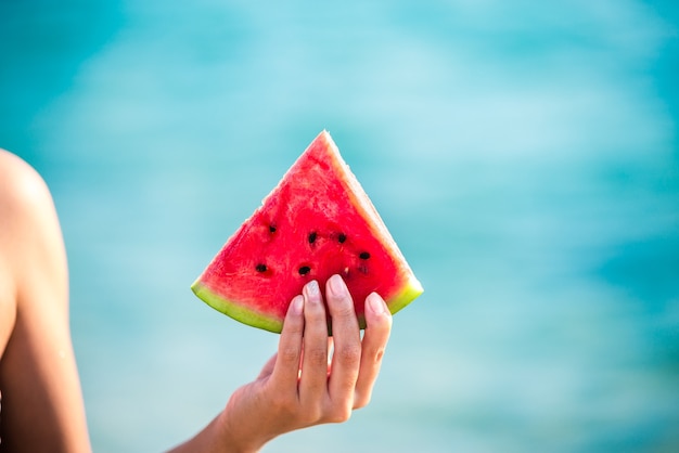 Wassermelonenscheibe in Frauenhand über Meer