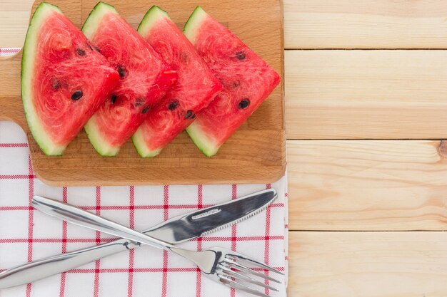 Wassermelonenscheiben auf einem Holzbrett, serviert mit Besteck und Serviette auf einem Holztisch