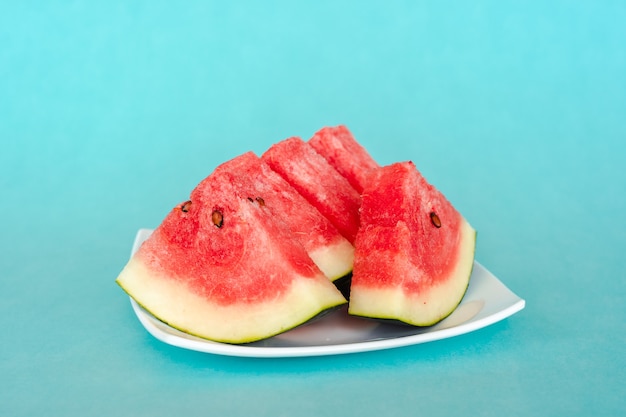 Wassermelonenscheiben auf einem Teller auf blauem Hintergrund. Saftiges frisches leckeres Sommerdessert. Stock Foto