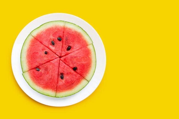 Wassermelonenscheiben in weißer Platte auf gelbem Hintergrund.