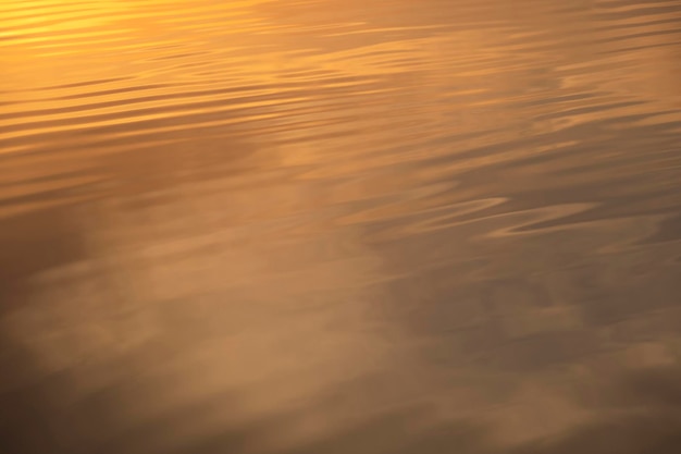 Wasseroberfläche bei Sonnenuntergang kräuselt sich und kleine goldene Wellen auf dem Wasserkopierraum