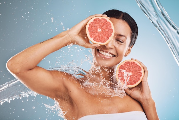 Wasserpflege und Grapefruit mit einer vorbildlichen schwarzen Frau im Studio auf blauem Hintergrund für Hygiene oder Flüssigkeitszufuhr Gesicht Schönheit und Obst mit einer attraktiven jungen Frau, die in einer Dusche posiert oder putzt