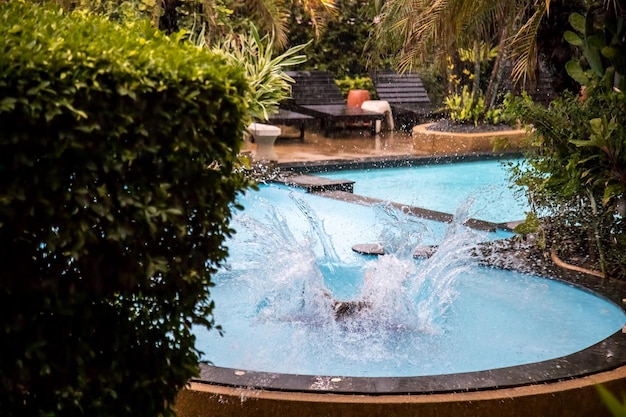 Wasserspritzer nach dem Sprung in ein tropisches Freibad bei strömendem Regen