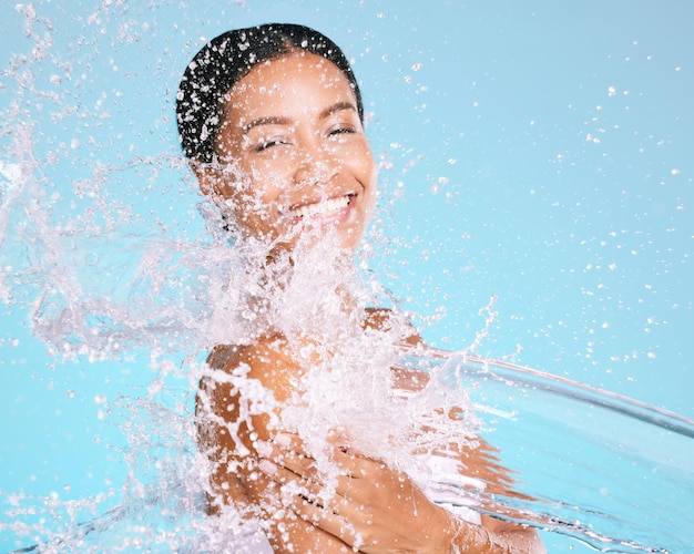 Foto wasserspritzer und schwarze frau, die ihren körper für schönheitshautpflege und selbstpflege reinigt, isoliert im blauen hintergrund des studios porträtmodell und junge weibliche waschhaut für hygiene, aqua und flüssigkeitszufuhr