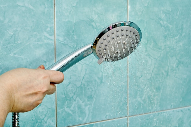 Wasserstrahlen laufen vom Duschkopf, der von Frau in der Hand gehalten wird