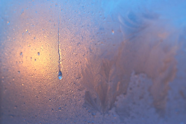 Wassertropfen auf dem Milchglas des Fensters Bunte Nahaufnahme mit warmem Licht des Sonnenuntergangs Winterhintergrund