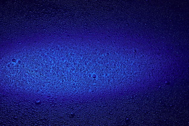 Wassertropfen auf schwarzem Glas. Hintergrund mit dunklem Blau beleuchtet