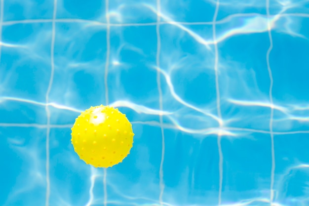 Wasservibrationen im Schwimmbad mit Sonnenreflexion und gelbem Ball zum Spielen. blaue Schwimmbadoberfläche, Wasser im Schwimmbad. Flache Lage, Draufsicht