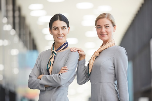 Wast up retrato de dos elegantes asistentes de vuelo y sonriendo mientras posa en el aeropuerto