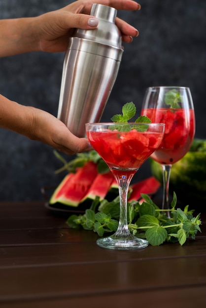 Watermelon Alcoholik oder alkoholfreier Cocktail mit Minze und Frauenhand mit Shaker auf dunklem Hintergrund
