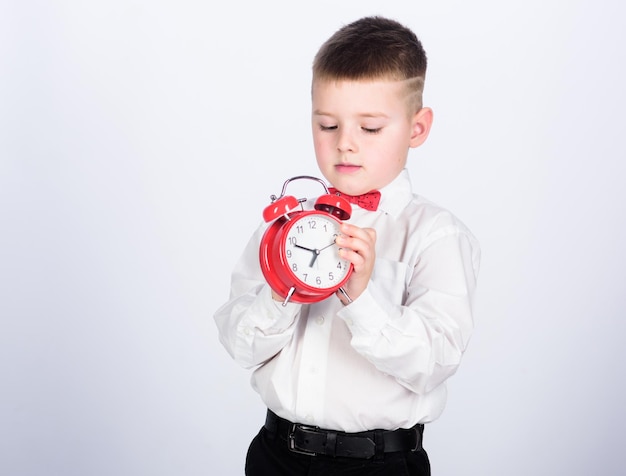 Wecker einrichten Kind kleiner Junge hält rote Uhr Es ist Zeit Zeitplan und Timing Morgenroutine Schuljunge mit Wecker Kind entzückender Junge weißes Hemd rote Fliege Entwickeln Sie Selbstdisziplin