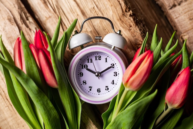 Wecker in Tulpenblumen auf Holzhintergrund Konzept der Zeit als Geschenk Herzlichen Glückwunsch zum Frühlingsanfang