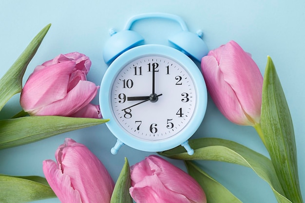 Wecker mit rosa Tulpen auf blauem Hintergrund