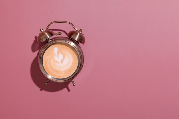 Wecker mit schaumigem Kaffee und Muster. Harte Schatten. Morgenaufgang mit Kaffee zum Frühstückskonzept mit Kopierraum