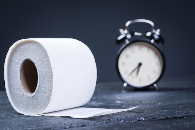 Wecker mit Toilettenpapier auf einem schwarzen Holztisch