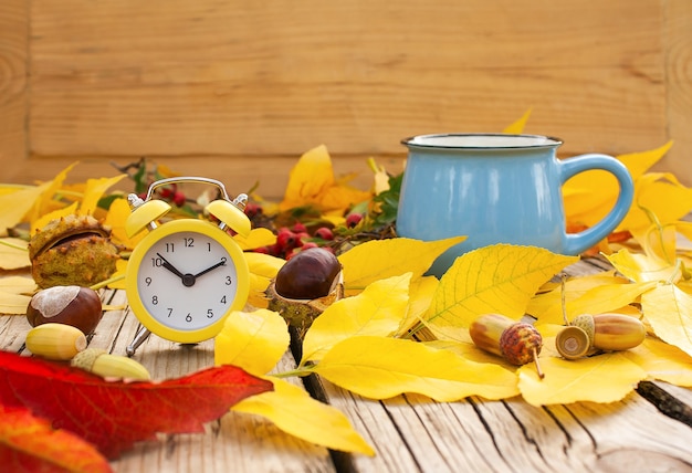 Wecker, Tasse und Herbstlaub auf einem alten Holztisch