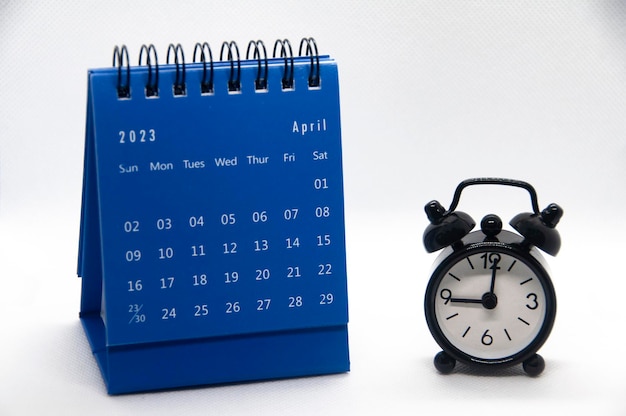 Wecker zeigt auf 9 Uhr mit Kalender April 2023 auf weißem Hintergrund Zeit- und Kalenderkonzept und Kopierbereich