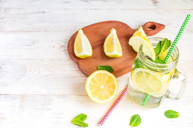 Weckglasglas selbst gemachte Limonade mit Zitronen, Minze und Grünbuchstroh auf hölzernem rustikalem Hintergrund. Erfrischendes Sommergetränk.