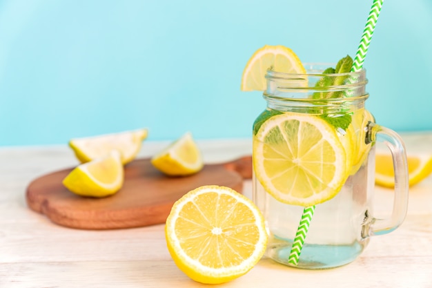 Weckglasglas selbst gemachte Limonade mit Zitronen-, Minzen- und Grünbuchstroh auf hölzerner rustikaler Tabelle und blauem Hintergrund.