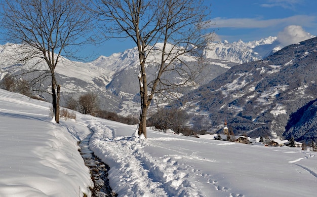 Weg auf dem Schnee mit schöner Aussicht auf schneebedeckte Berge und Alpendorf