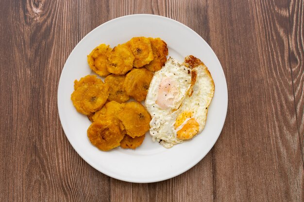 Wegerich und Spiegeleier Typisch kubanisches und karibisches Essen in weißer Platte auf Holztisch serviert