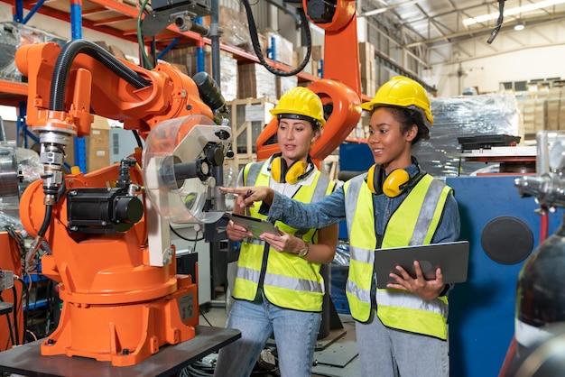 Weibliche Automatisierungsingenieure, die einen Laptop zur Inspektion neuer Schweißroboterarmmaschinen in der Fabrik verwenden