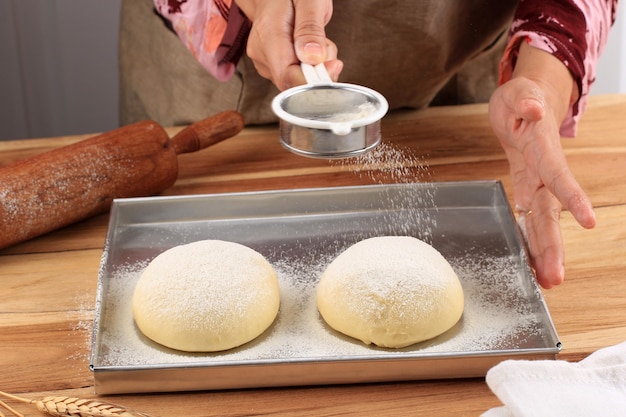 Weibliche Bäcker halten Sieb, das rohen Brotteig mit Mehl beschichtet, Backprozess, der Milchherdbrot oder Mirukuhasu, japanisches weißes flauschiges Brot macht