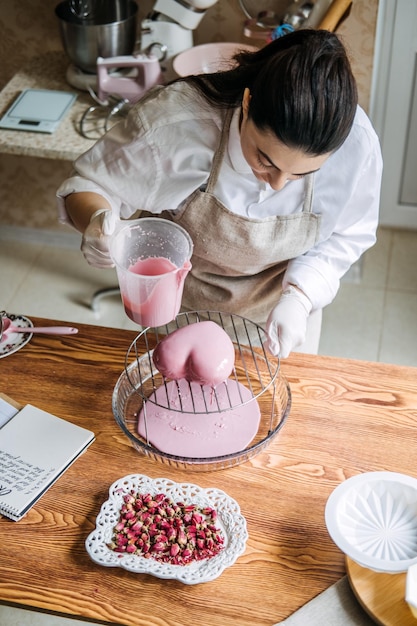 Weibliche Bäckerin macht einen perfekten maßgeschneiderten rosa Herzformkuchen in der Küche Bäckerei Online-Kuchenladen maßgeschnitten