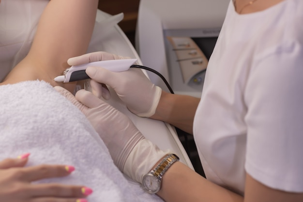 Weibliche Beine auf violettem Blatt während der Epilation durch eine professionelle Kosmetikerin in Handschuhen. Spa, Schönheitsindustrie, Behandlung in der Klinik, Elektrolyse.