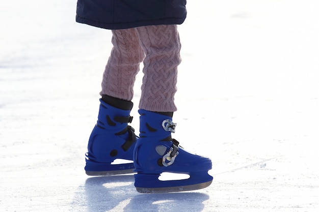 Weibliche Beine beim blauen Schlittschuhlaufen auf der Eisbahn