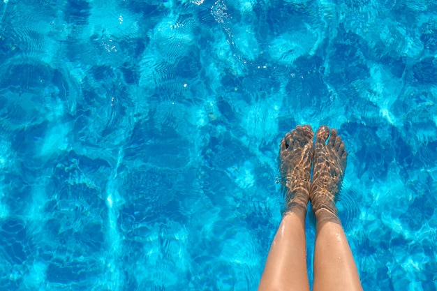Weibliche Beine im Poolwasser im Sommer