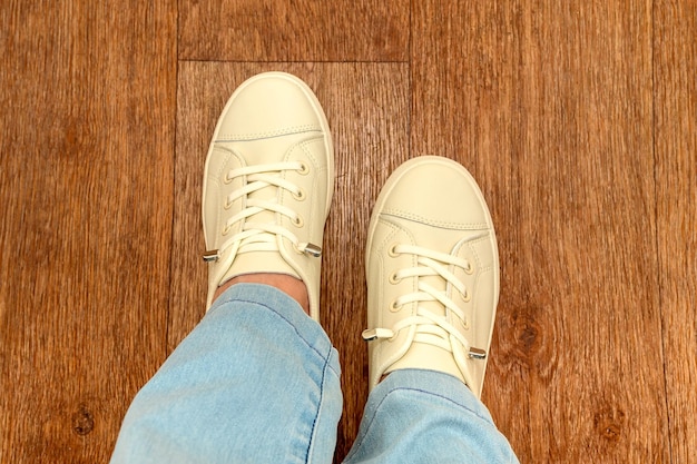 Weibliche Beine in blauen Jeans und weißen Sportschuhen mit weißen Schnürsenkeln stehen auf dem Boden