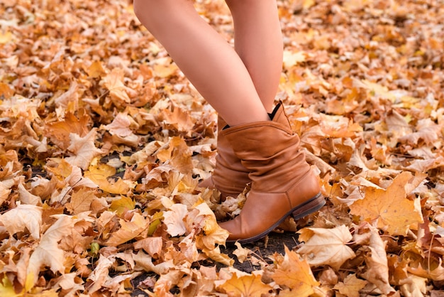 Weibliche Beine in braunen Stiefeln. Gelbes Laub unter den Füßen. Herbstkonzept