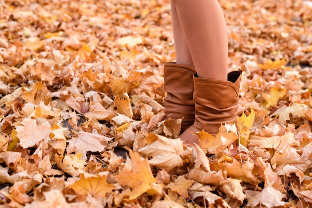 Weibliche Beine in braunen Stiefeln. Gelbes Laub unter den Füßen. Herbstkonzept