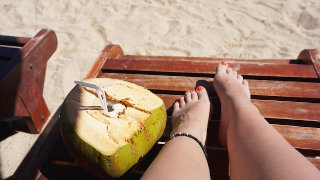 Weibliche beine und kokosnuss trinken am strand, reisen und entspannen