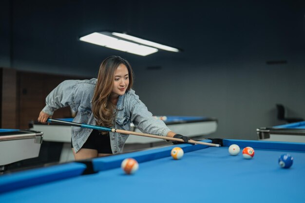 Foto weibliche billardspielerin, die den billardball ernsthaft mit dem cue-stick im billardstudio steckt