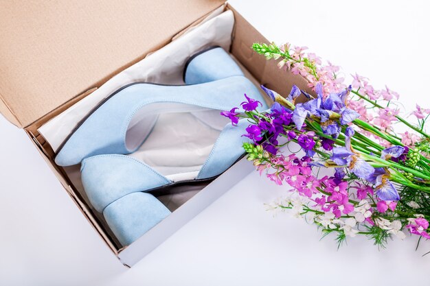 Weibliche blaue Hochzeitsschuhe im Kasten mit Blumen auf Weiß