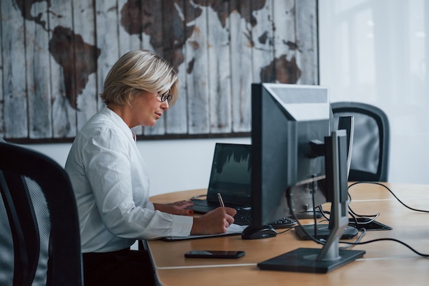 Weibliche Börsenmaklerin in formeller Kleidung arbeitet im Büro mit Finanzmarkt.