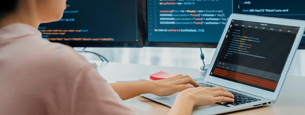 Weibliche Entwicklerin, die auf einem Laptop programmiert, während ein Computer ein Programm anzeigt.