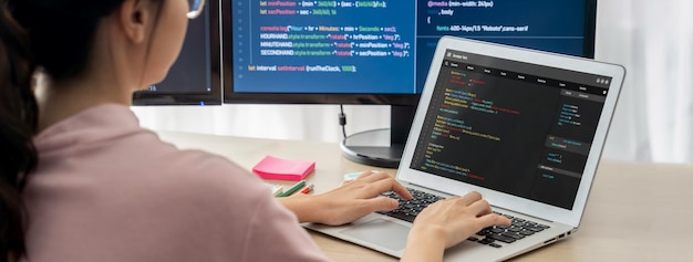 Weibliche Entwicklerin, die auf einem Laptop programmiert, während ein Computer ein Programm anzeigt.