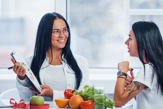 Weibliche Ernährungsberaterin berät Patienten drinnen im Büro, indem sie Notizblock verwendet.