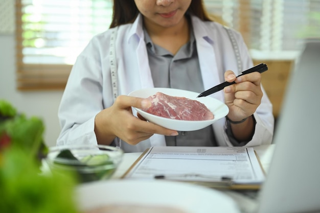 Weibliche Ernährungswissenschaftlerin in weißem Mantel ruft Patienten an und gibt Online-Konsultationen über einen Laptop