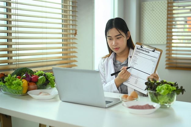 Weibliche Ernährungswissenschaftlerin in weißem Mantel ruft Patienten an und gibt Online-Konsultationen über einen Laptop
