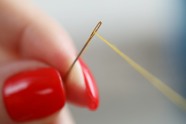 Weibliche Finger mit Maniküre halten eine Nadel und Fadennahaufnahme dringende Kleidung zum Selbermachen