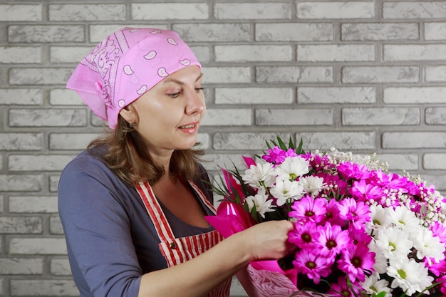 Weibliche Floristin bindet eine Schleife an einem Blumenstrauß, der in Bastelpapier auf der Desktop-Oberseite eingewickelt ist