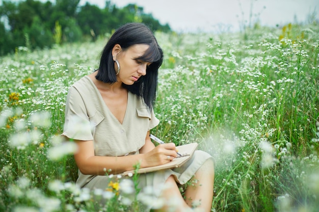 Weibliche Frau mit Federschreiben oder Malhandschrift auf Notizbuch auf blühender Blumenwiese
