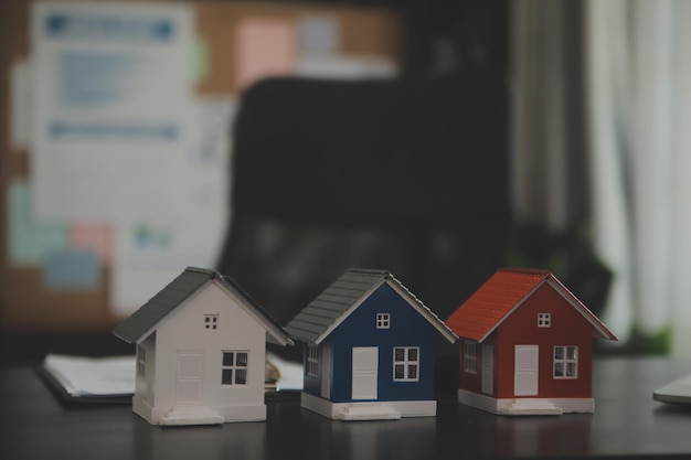 Weibliche Frauenhände, die ein kleines weißes Miniatur-Spielzeughaus des Hausmodells halten Hypotheken-Sachversicherungstraumumzug und Immobilienkonzept