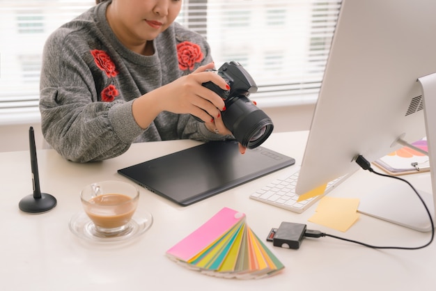 Weibliche freiberufliche Fotografin, die Fotos auf einer Digitalkamera überprüft, während sie am Tisch in der Workstation sitzt